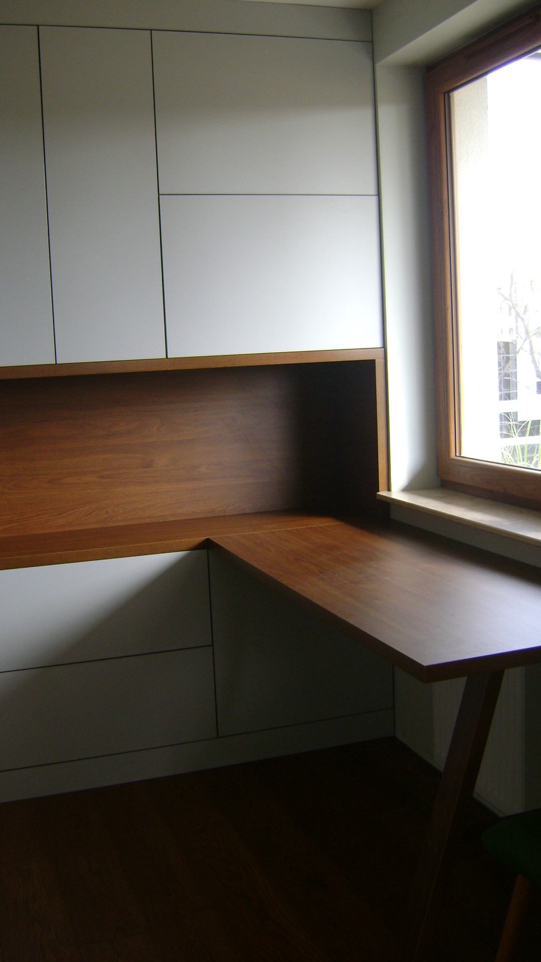 Białe szafki z drewnianym blatem roboczym narożnym, dopasowane do okna, widok z dołu