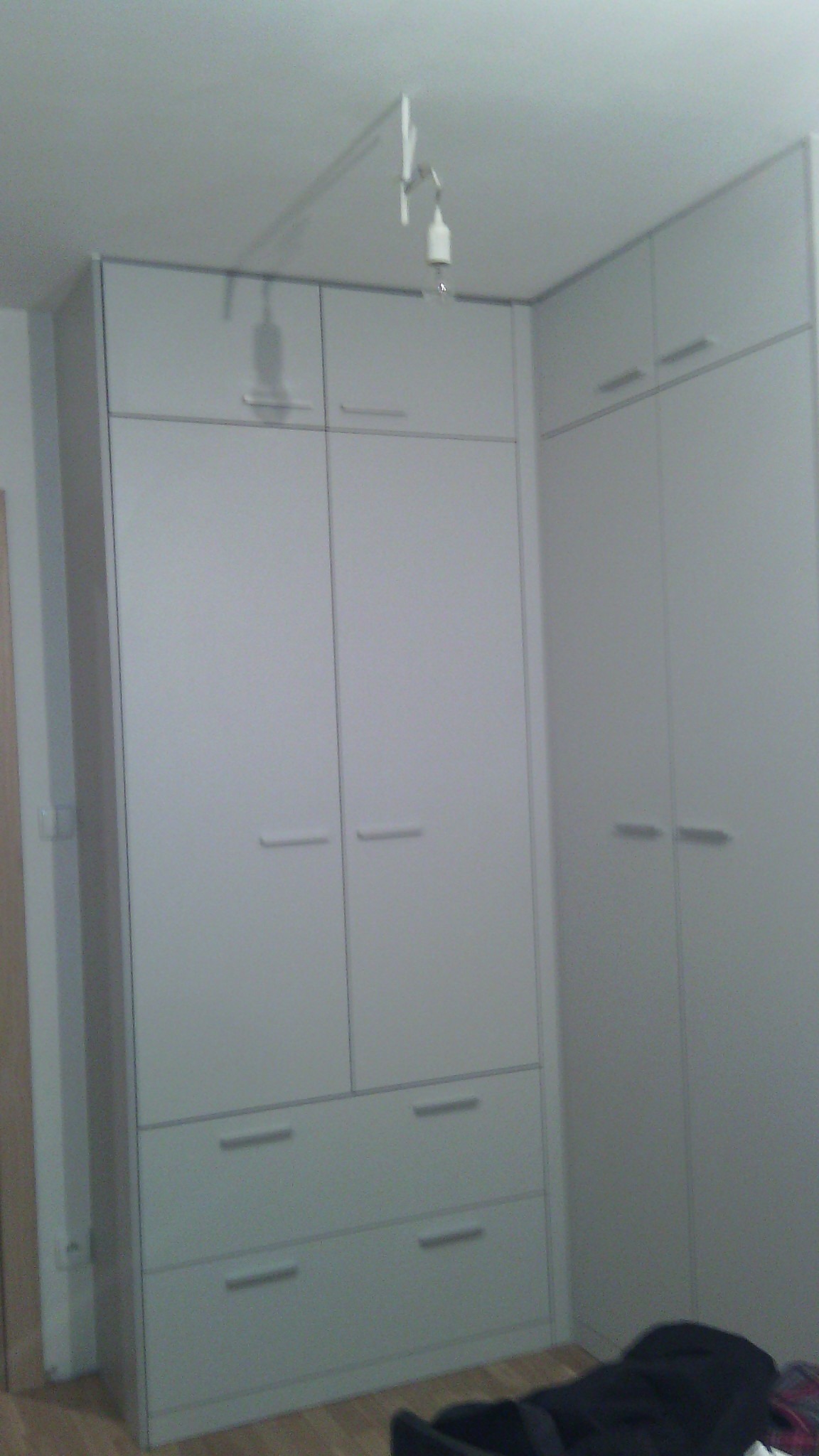 Biała szafa wnękowa z szufladami i górnymi szafkami, oświetlona lampą na wysięgniku, widok z dołu.