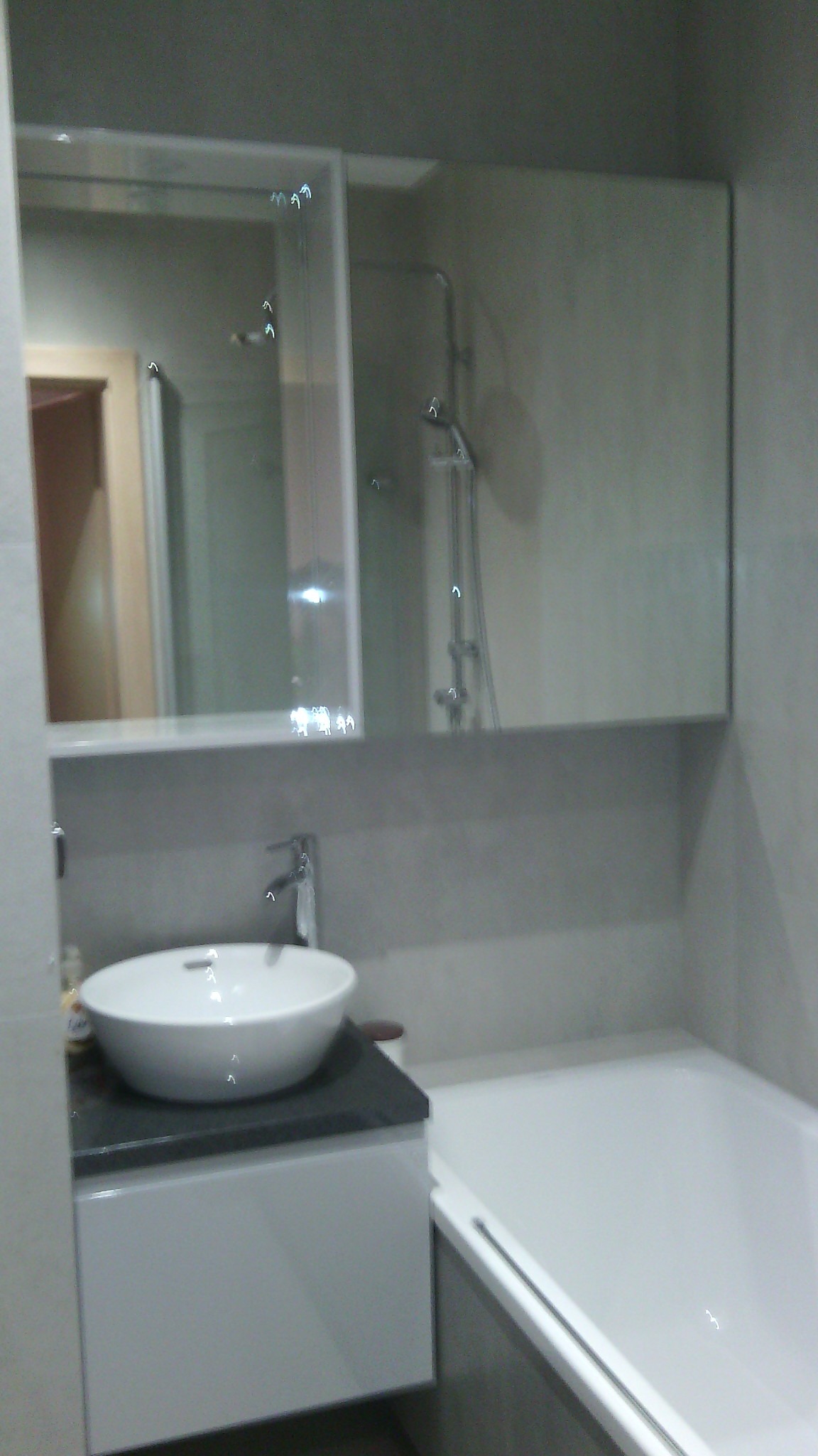 Nowoczesna łazienka z umywalką nablatową na szafce z szarym blatem, duże lustro z odbiciem kabiny prysznicowej, obok wanna.