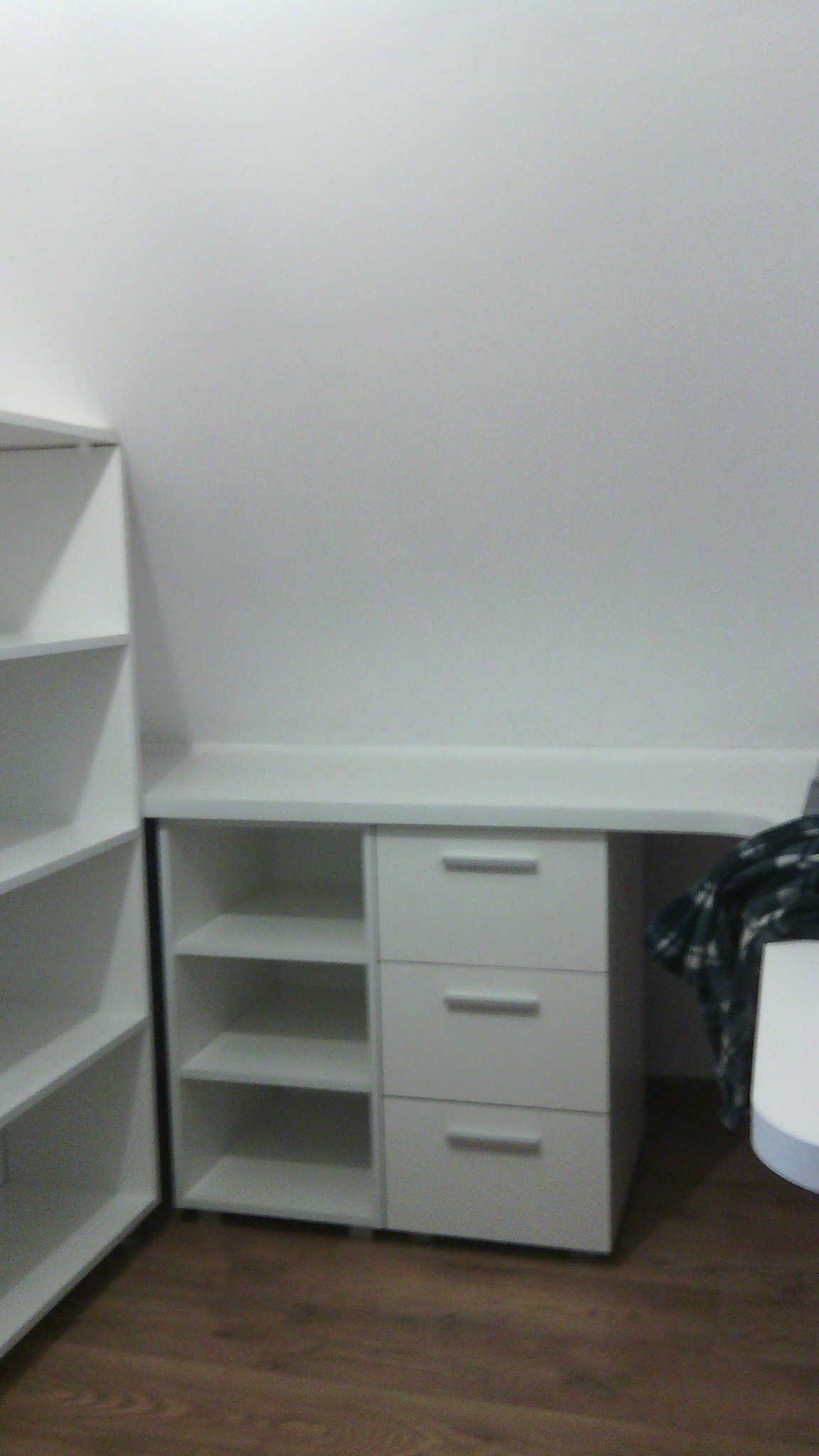 Biała, zabudowana szafa z szufladami i półkami, wkomponowana we wnękę pokoju z drewnianą podłogą.