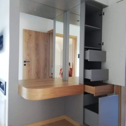 GCK Meble Na Wymiar - Szara szafa wnękowa z lustrami i drewnianym blatem, otwarte szuflady z drewnianym wnętrzem, widoczne drzwi w tle.