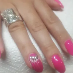 Dłoń z pomalowanymi na różowo paznokciami, jeden z nich ozdobiony białymi wzorami i trzema srebrnymi dżetami, na palcu serdecznym duży srebrny pierścień.