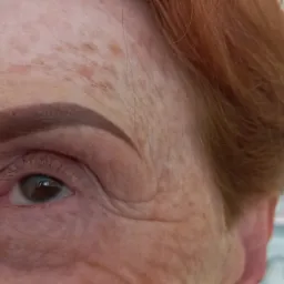 Zbliżenie na oko kobiety z rudymi włosami i świeżo wykonanym makijażem permanentnym brwi w odcieniu brązu.