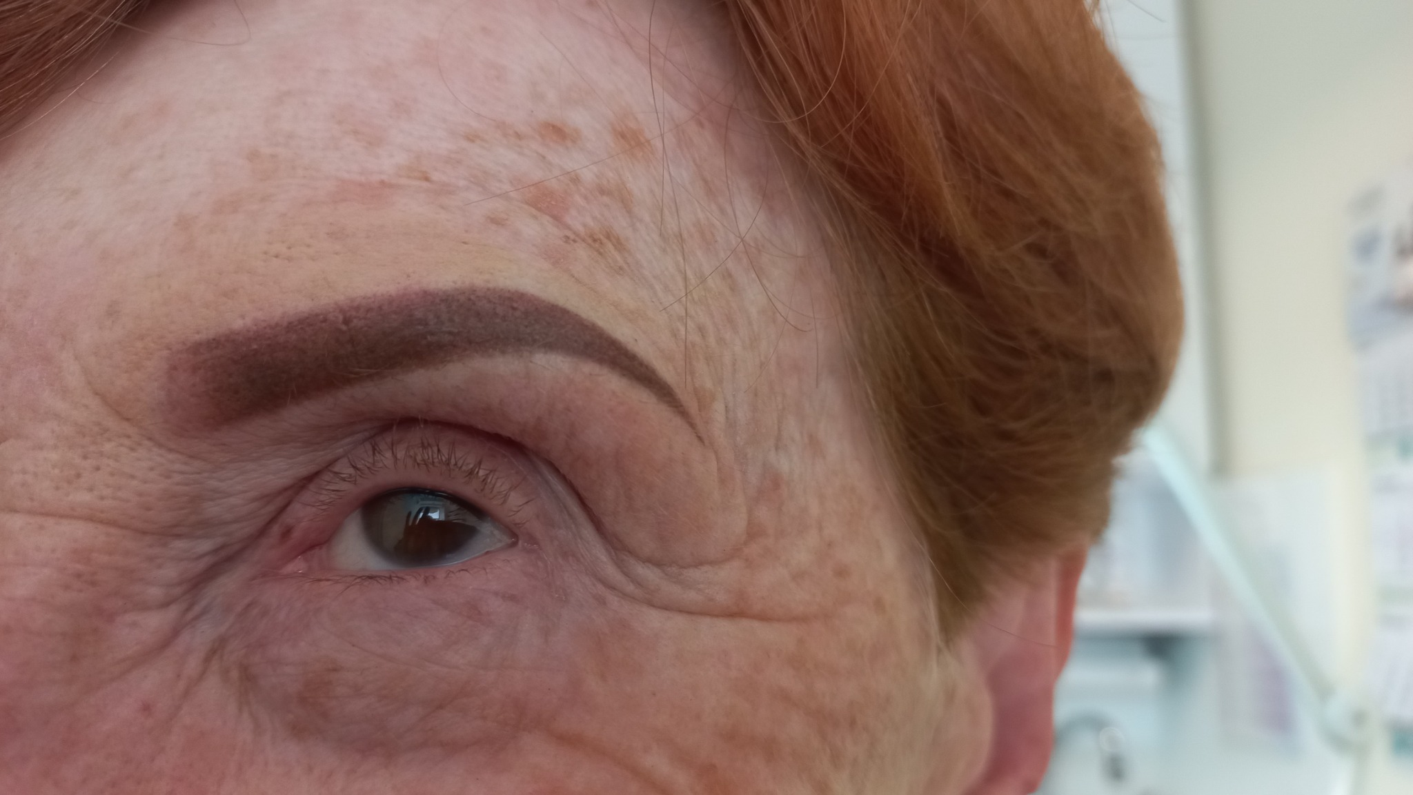 Zbliżenie na oko kobiety z rudymi włosami i świeżo wykonanym makijażem permanentnym brwi w odcieniu brązu.