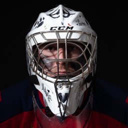 Marta Piątek Fotografia - Portret hokejowego bramkarza w masce CCM z autografami i rysunkami, w barwach klubowych na czarnym tle.