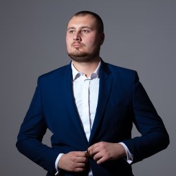 Marta Piątek Fotografia - Mężczyzna w granatowym garniturze zapinający guzik, z lekkim zarostem i spojrzeniem w bok na szarym tle.