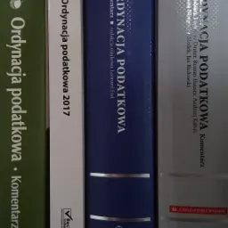 Półka z książkami prawniczymi, głównie komentarze do Ordynacji Podatkowej różnych wydań i autorów, widoczne grzbiety książek w kolorach zielonym, białym, niebieskim i srebrnym.