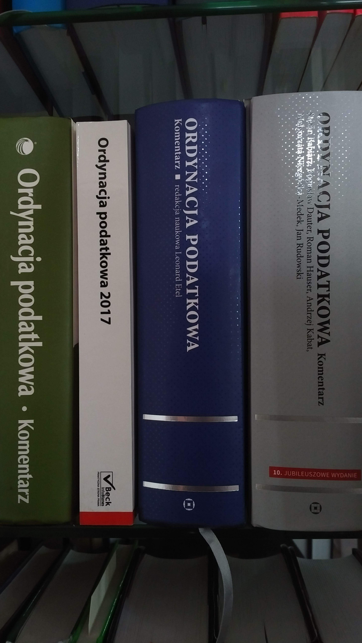 Półka z książkami prawniczymi, głównie komentarze do Ordynacji Podatkowej różnych wydań i autorów, widoczne grzbiety książek w kolorach zielonym, białym, niebieskim i srebrnym.
