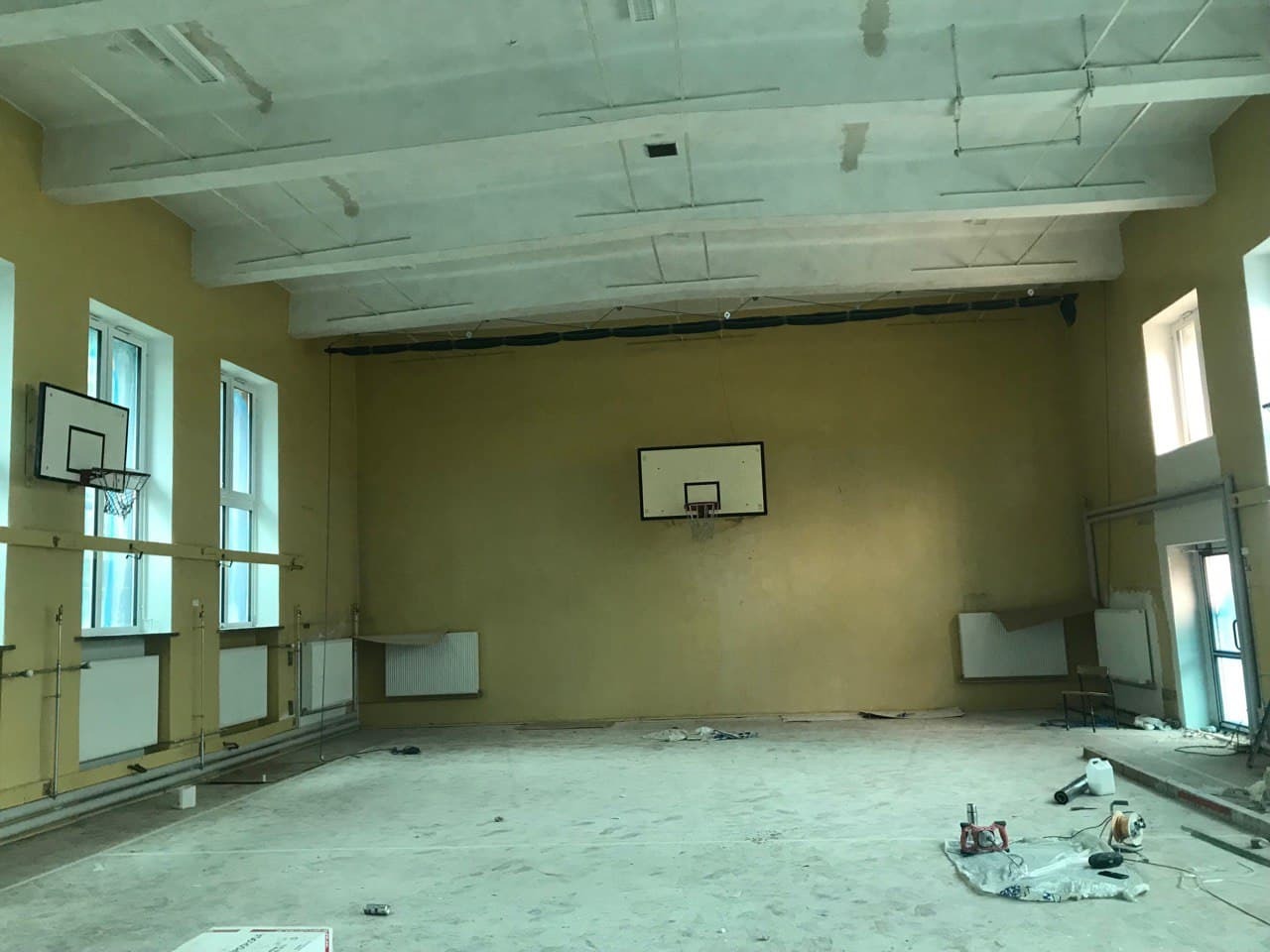 Wnętrze remontowanej sali gimnastycznej w Białymstoku z widocznymi śladami prac malarskich na ścianach i suficie, oraz sprzętem budowlanym leżącym na podłodze.