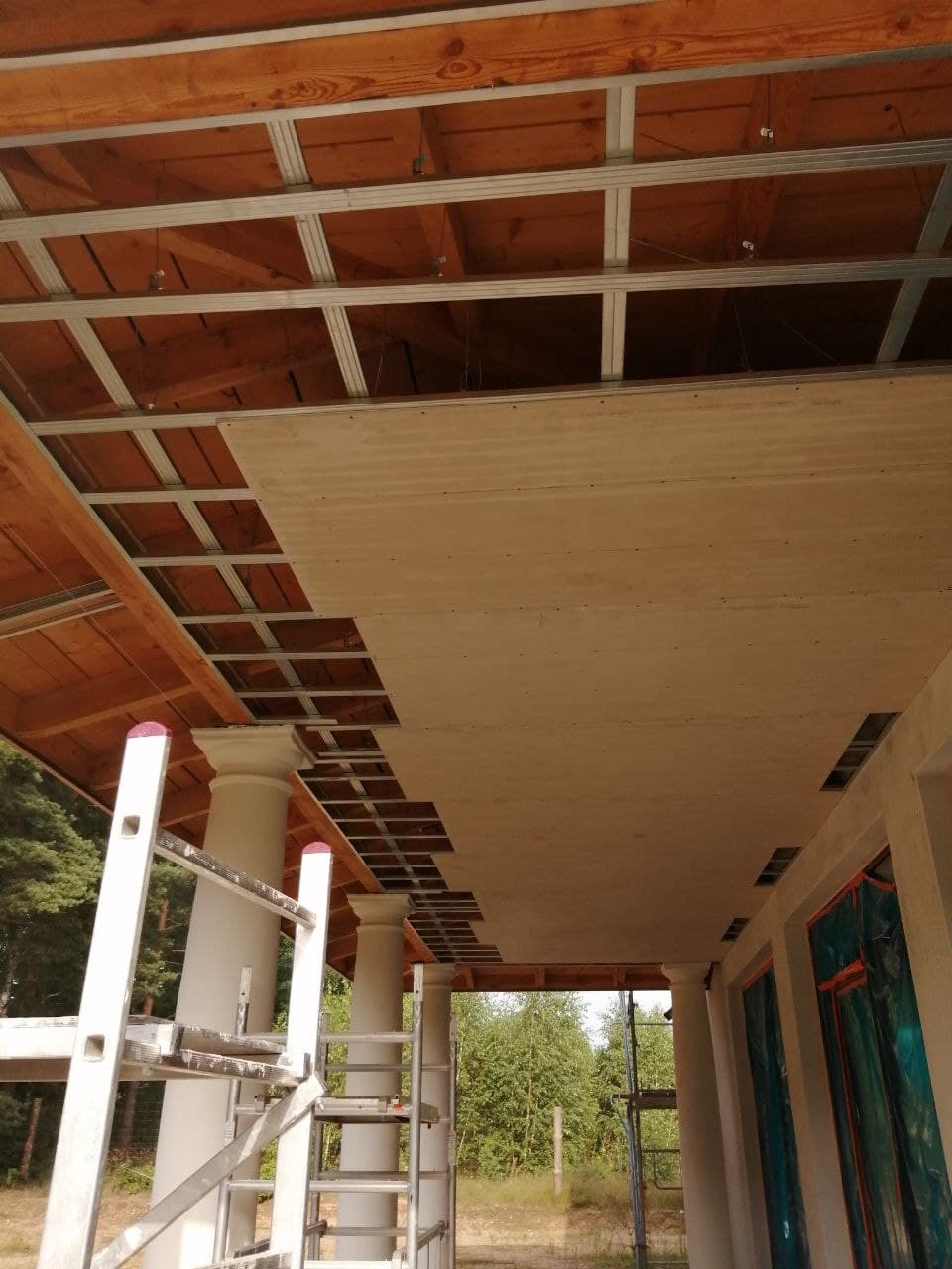 Montaż sufitu podwieszanego: widok na konstrukcję metalową i częściowo zamontowane płyty, z widocznymi kolumnami i drabiną w tle.