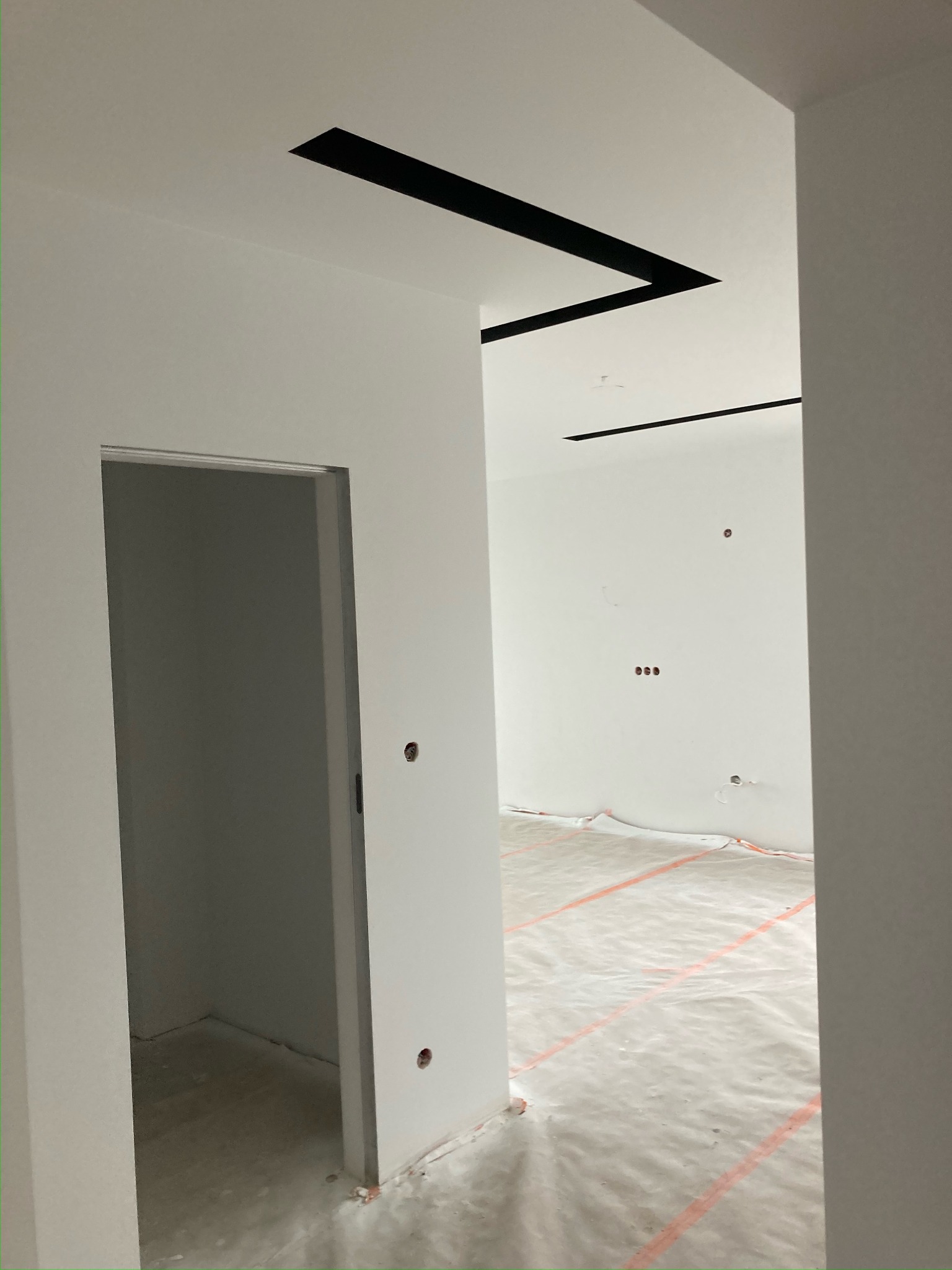 Wnętrze w Krakowie po przygotowaniu do prac wykończeniowych, zabezpieczona podłoga folią, białe ściany z czarnymi elementami dekoracyjnymi na suficie, widoczne otwory po gniazdkach elektrycznych.