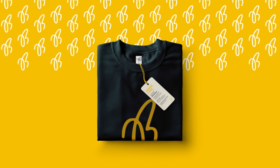 Złożona czarna koszulka z żółtym nadrukiem banana i metką na żółtym tle z powtarzającym się wzorem banana.