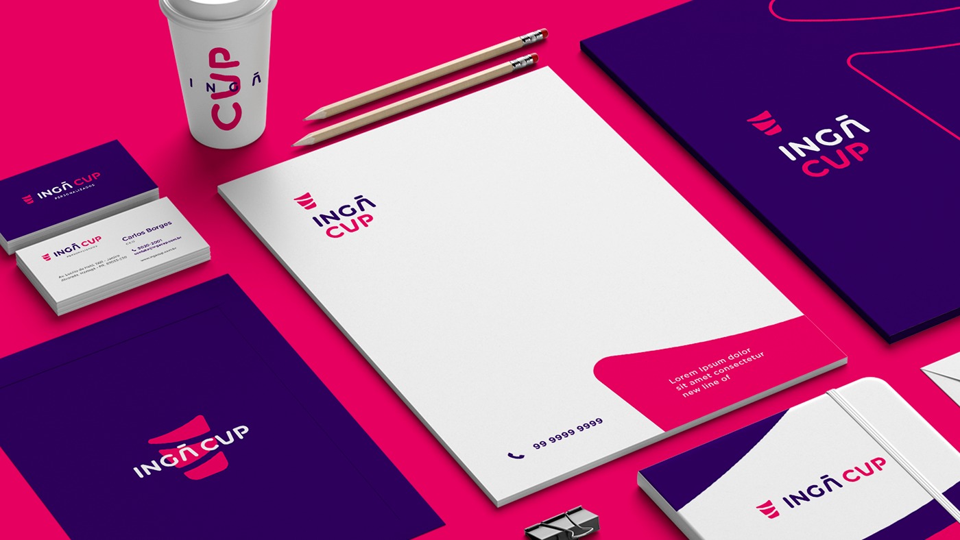 Zestaw materiałów firmowych z logo Inga Cup: wizytówki, papier firmowy, notes, kubek, folder, dwa ołówki, spinacz biurowy na różowym tle.