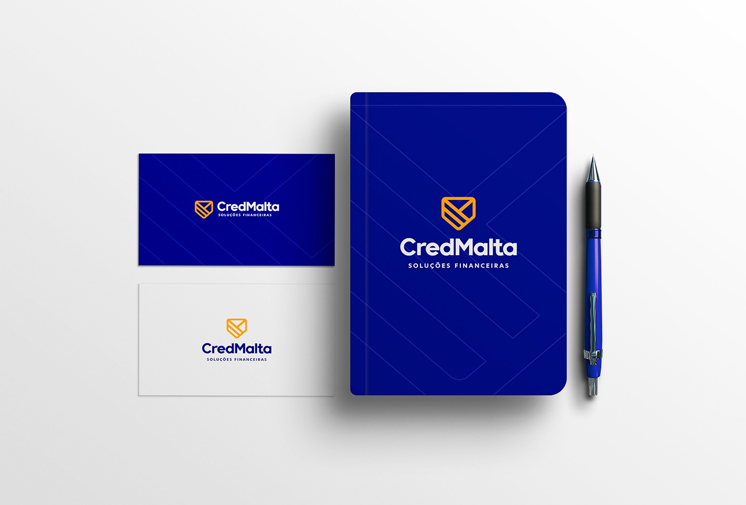Wizytówki, notes w kolorze granatowym i długopis prezentujące identyfikację wizualną firmy CredMalta z żółtym logo na białym tle.