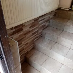 Wyłożone płytkami schody z brązową mozaiką na ścianie, widoczne z perspektywy od dołu, przy białym grzejniku.