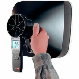 Pomiar przepływu powietrza anemometrem z wyświetlaczem cyfrowym, urządzenie przyłożone do wylotu wentylacyjnego, widoczna dłoń operatora w koszuli w kratę.