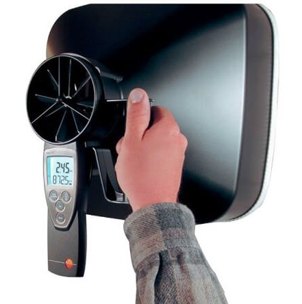 Pomiar przepływu powietrza anemometrem z wyświetlaczem cyfrowym, urządzenie przyłożone do wylotu wentylacyjnego, widoczna dłoń operatora w koszuli w kratę.