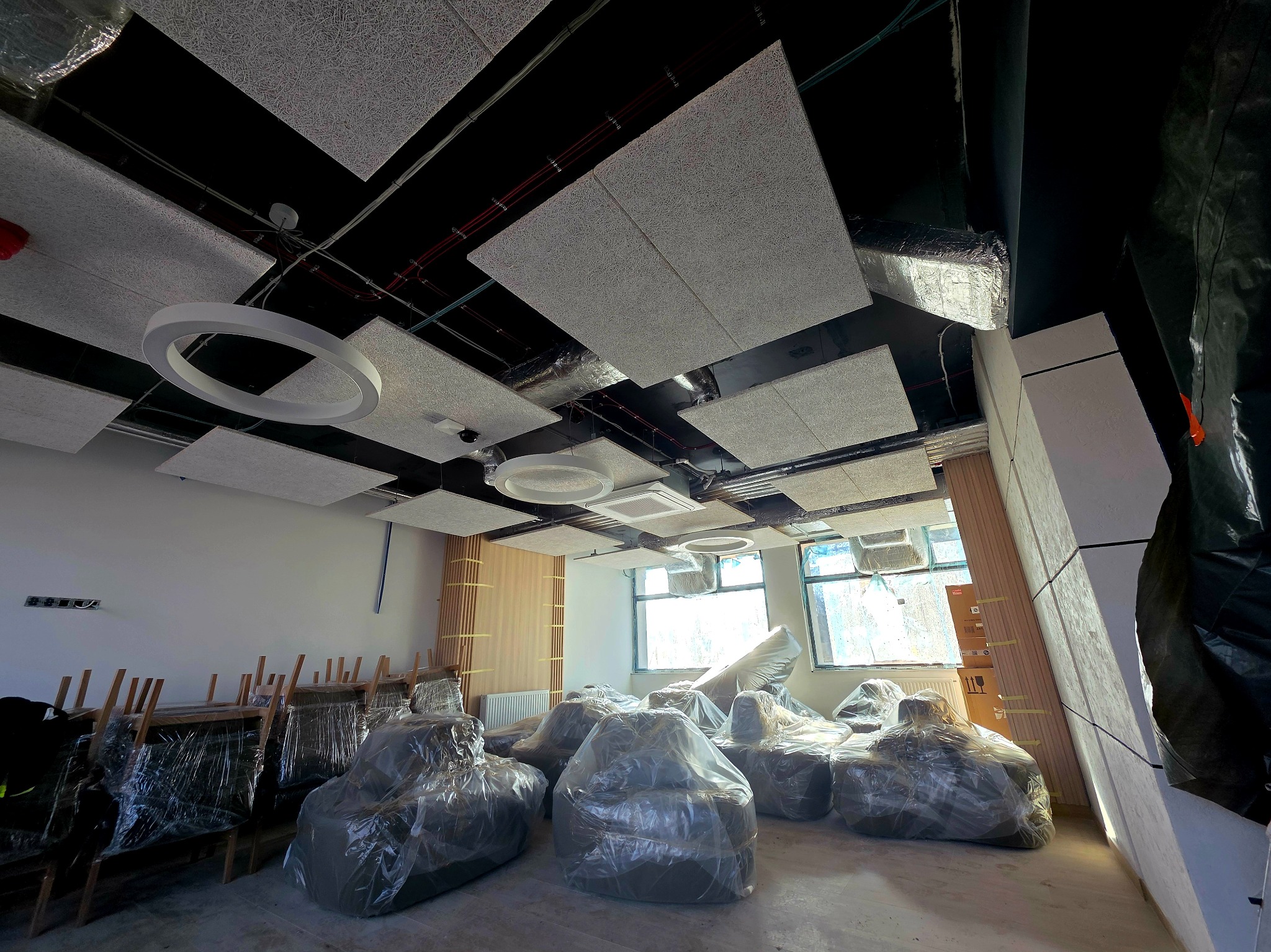 Montaż sufitu akustycznego z oświetleniem w nowym biurze. Meble zabezpieczone folią. Widoczne panele i lampy. Jasne wnętrze w trakcie wykończenia.