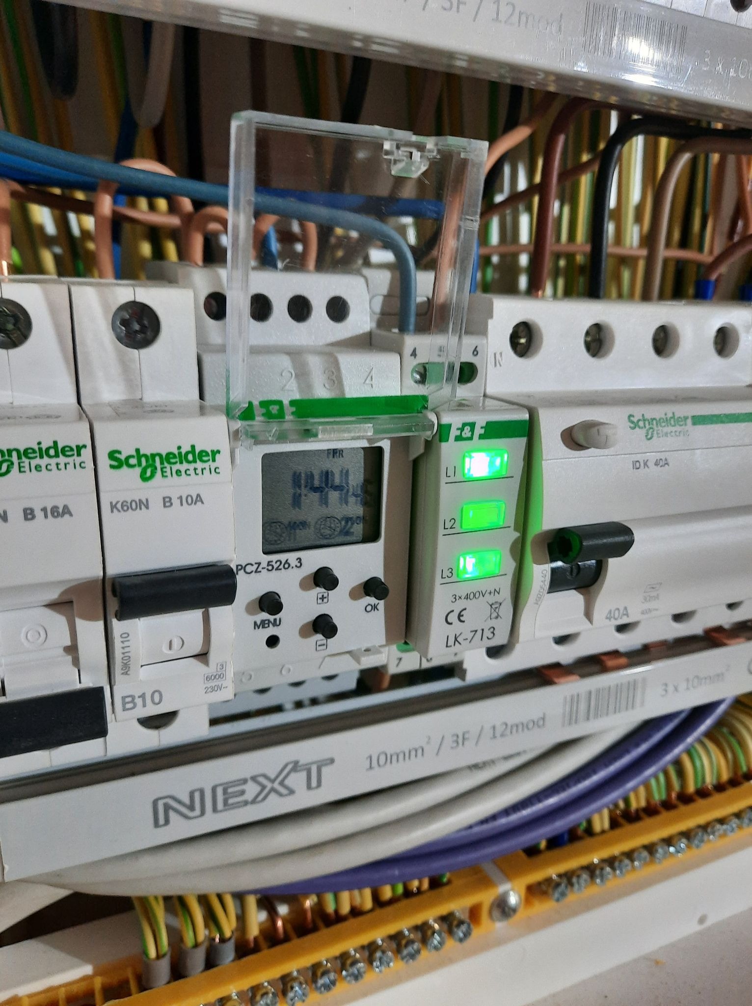 Zbliżenie na panel elektryczny z wyłącznikami Schneider Electric, timerem PCZ-526.3 i listwą zaciskową, widoczne przewody w różnych kolorach.