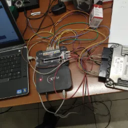 Laptop z uruchomionym oprogramowaniem diagnostycznym, interfejs do programowania sterowników silnika (ECU) podłączony przewodami do komputera i modułu sterującego Bosch, widoczne oznaczenia...