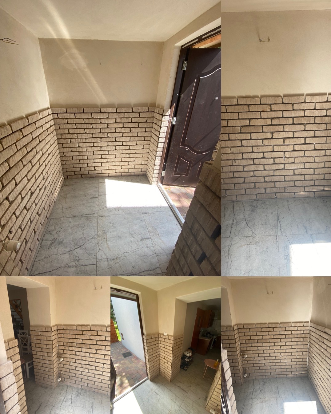 Korytarz z częściowo wykończonymi ścianami z cegły klinkierowej, jasna marmurowa podłoga, widoczne ślady po instalacjach na ścianie, drzwi wejściowe w tle.