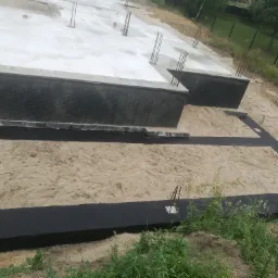 Wylany fundament z hydroizolacją pionową i poziomą, wystające pręty zbrojeniowe, teren budowy.