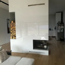 Nowoczesna ściana działowa z wnęką na drewno kominkowe i wbudowanym kominkiem, wykończona na wysoki połysk, widok z perspektywy salonu