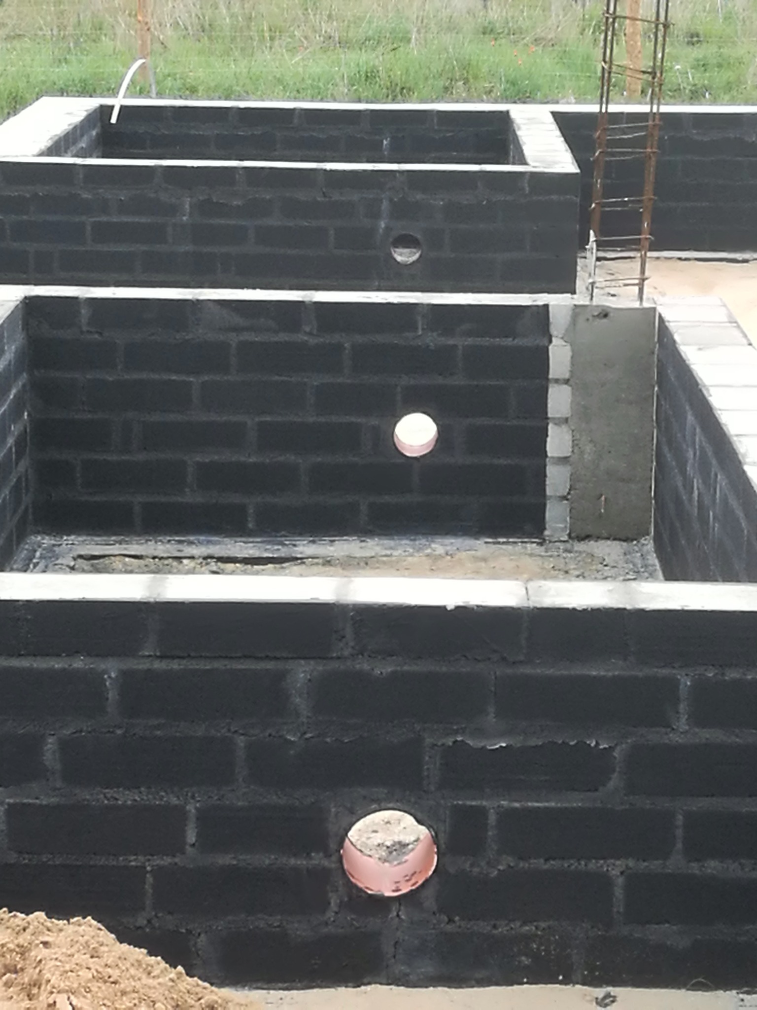 Wykop pod fundamenty z czarnych bloczków betonowych z widocznymi otworami na rury, realizacja w Żarach, zbrojenie wystaje z jednego z rogów.