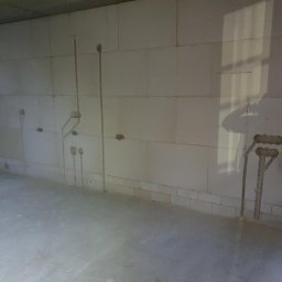 Firma Usługowa Work Service - Surowy stan pomieszczenia z białymi ścianami z betonu komórkowego, widoczne pionowe rury instalacji elektrycznej wystające ze ścian, przygotowane pod gniazdka i oświetlenie.