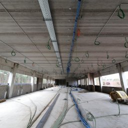 Firma Usługowa Work Service - Wnętrze hali w trakcie instalacji elektrycznej: koryta kablowe pod sufitem, wiązki przewodów na podłodze, widoczne okna i surowa konstrukcja budynku.