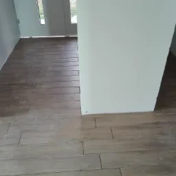 Ułożone panele podłogowe imitujące drewno w jasnym pomieszczeniu, widoczne fragmenty ścian i drzwi.