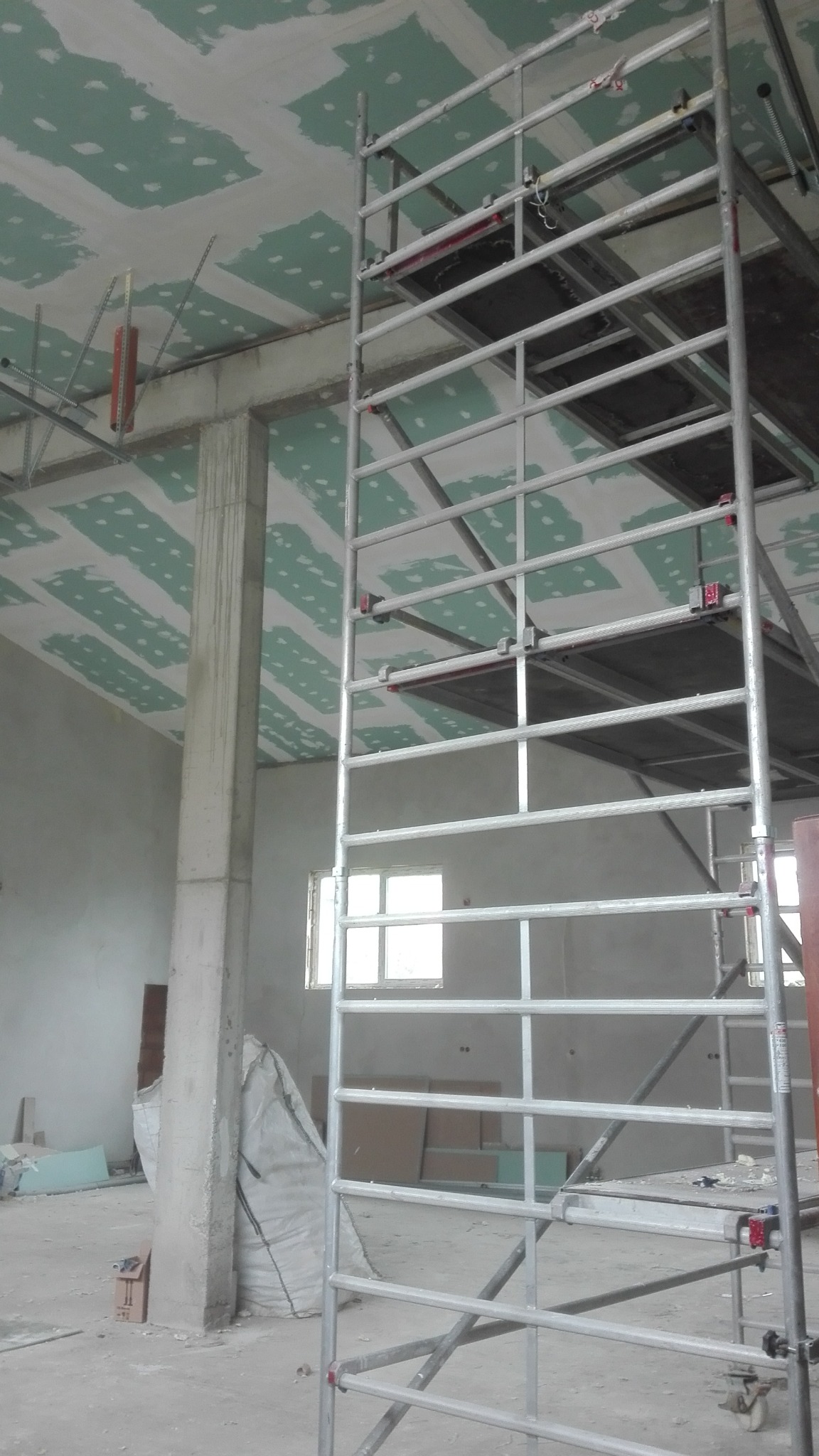 Wnętrze w Dzierżoniowie w trakcie prac wykończeniowych: widok na sufit z nałożoną gładzią szpachlową, metalowe rusztowanie i betonowy filar.