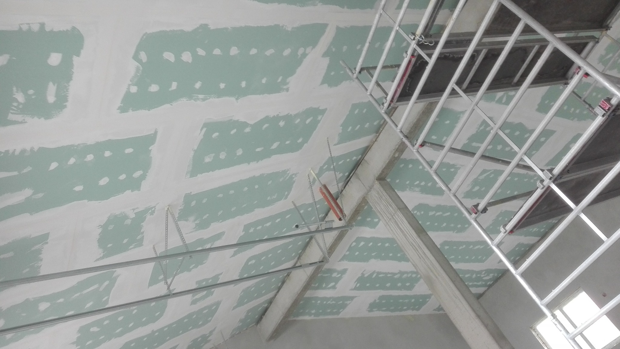 Sufit poddasza z zamontowanymi płytami gipsowo-kartonowymi, widoczne profile i rusztowanie, szpachlowane łączenia płyt.