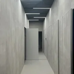 Szary korytarz biurowy z otwartymi drzwiami i panelami sufitowymi z oświetleniem LED.