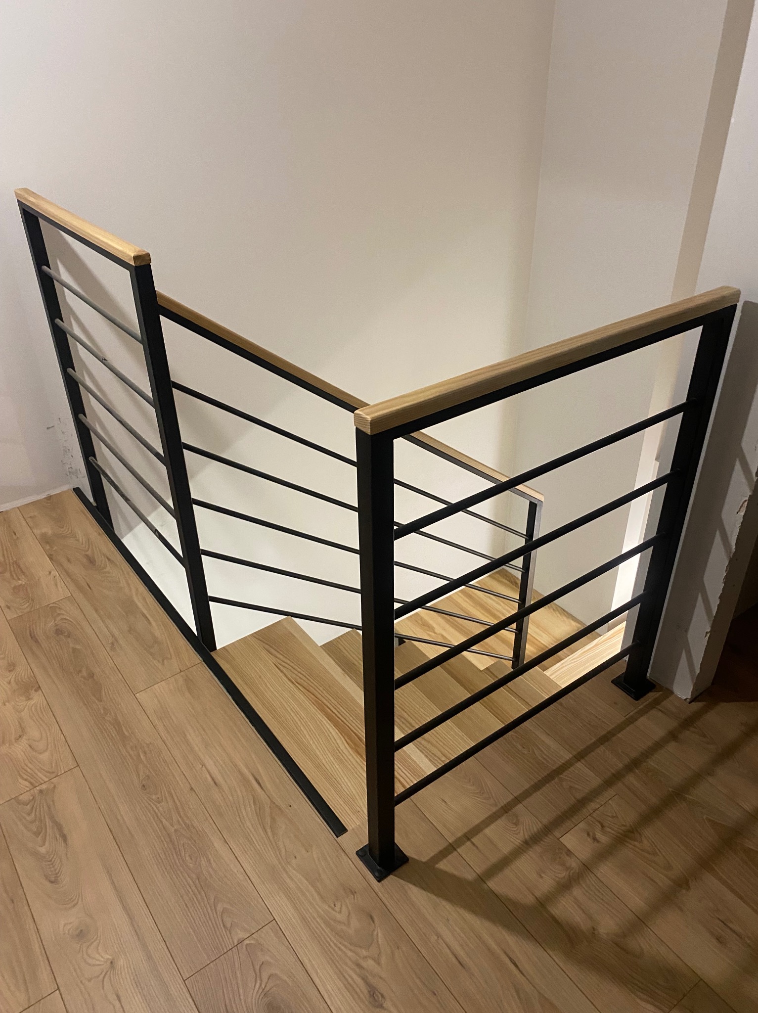 Nowoczesne schody z drewnianymi stopniami i czarną metalową balustradą z drewnianą poręczą, widok z góry, oświetlenie punktowe podkreśla fakturę drewna.