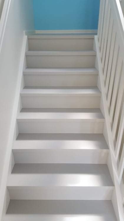 Białe schody z drewnianą balustradą, pomalowane na biało, z niebieskim fragmentem ściany widocznym u góry.