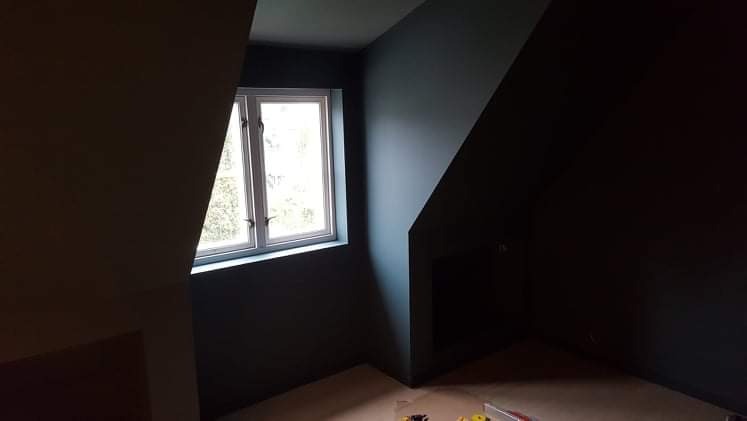 Poddasze po malowaniu na ciemny odcień szarości, widoczne okno z białymi ramami i fragment podłogi z narzędziami malarskimi.