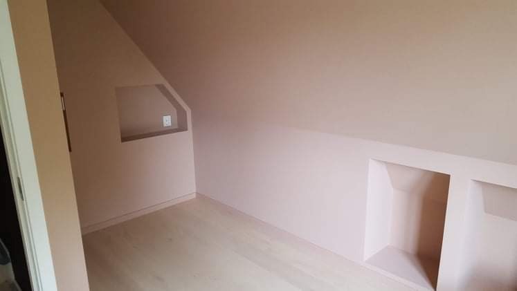 Poddasze po remoncie z wygładzonymi i pomalowanymi ścianami na delikatny róż, widoczne wnęki w ścianach i jasna drewniana podłoga.