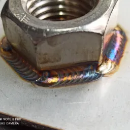 Szczegółowe zbliżenie na spawany gwintowany element z widocznymi tęczowymi przebarwieniami na spoinie.