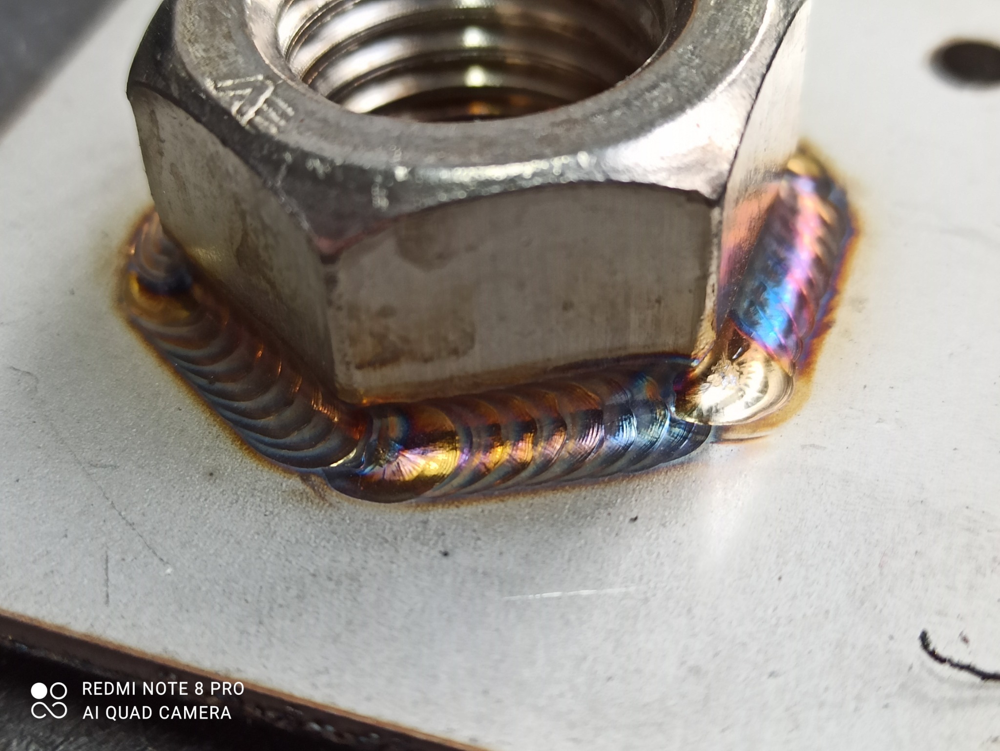 Szczegółowe zbliżenie na spawany gwintowany element z widocznymi tęczowymi przebarwieniami na spoinie.