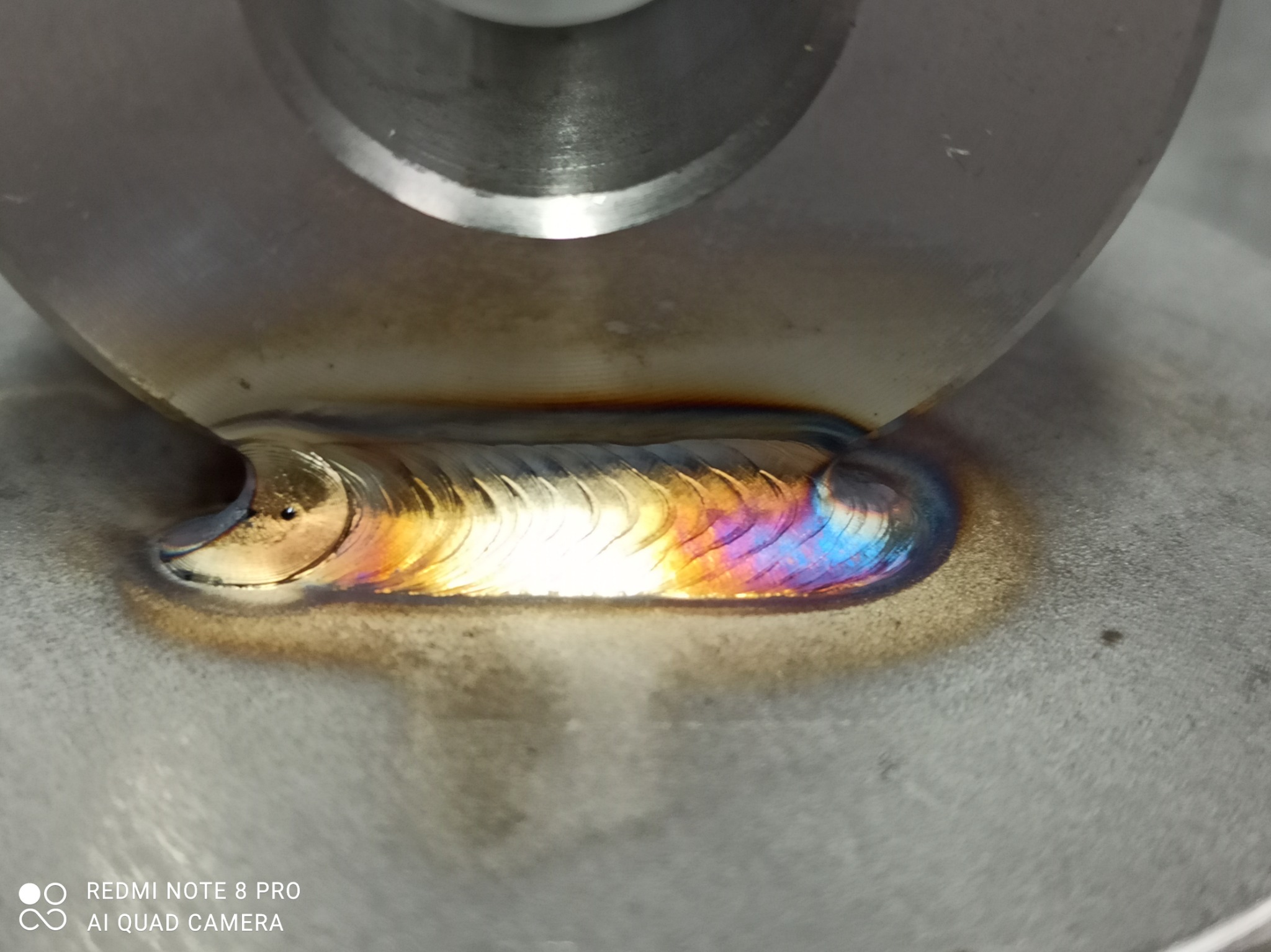 Spoina spawalnicza na metalowym elemencie, widoczne tęczowe przebarwienia po spawaniu, wykonane metodą TIG.