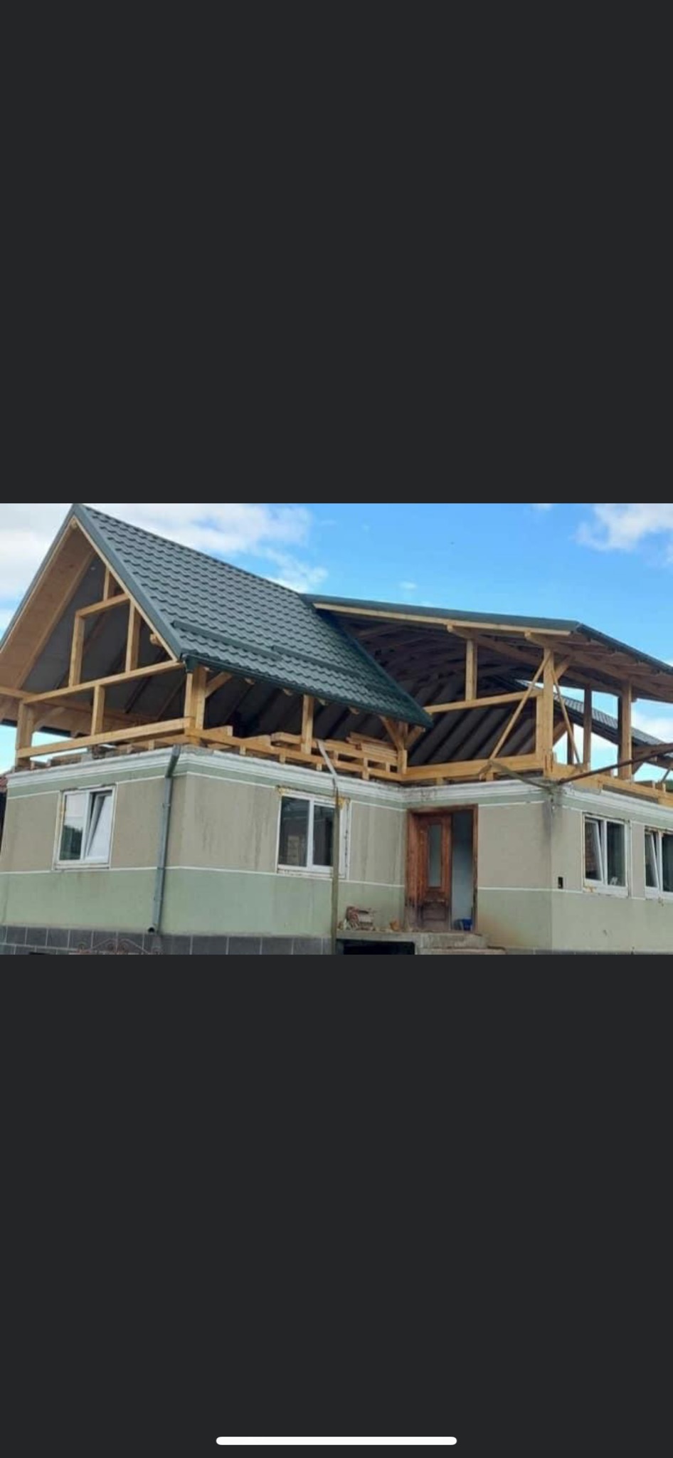 Dom w trakcie budowy z częściowo pokrytym zieloną blachą dachem i widoczną drewnianą konstrukcją więźby dachowej.