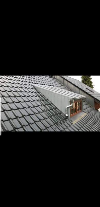 Dach pokryty ciemną dachówką ceramiczną z lukarną obłożoną blachą, widoczny system rynnowy odprowadzający wodę.