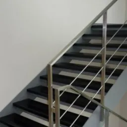 Nowoczesne schody wewnętrzne z czarnymi stopniami i metalową, minimalistyczną balustradą ze stali nierdzewnej, widok z dołu.