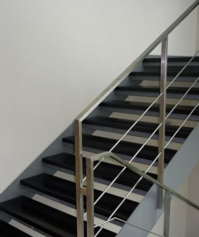 Nowoczesne schody wewnętrzne z czarnymi stopniami i metalową, minimalistyczną balustradą ze stali nierdzewnej, widok z dołu.