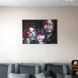 Abstrakcyjny portret rodzinny z użyciem czerwieni, bieli i czerni, wiszący nad szarą kanapą z poduszkami i pluszową pszczołą.