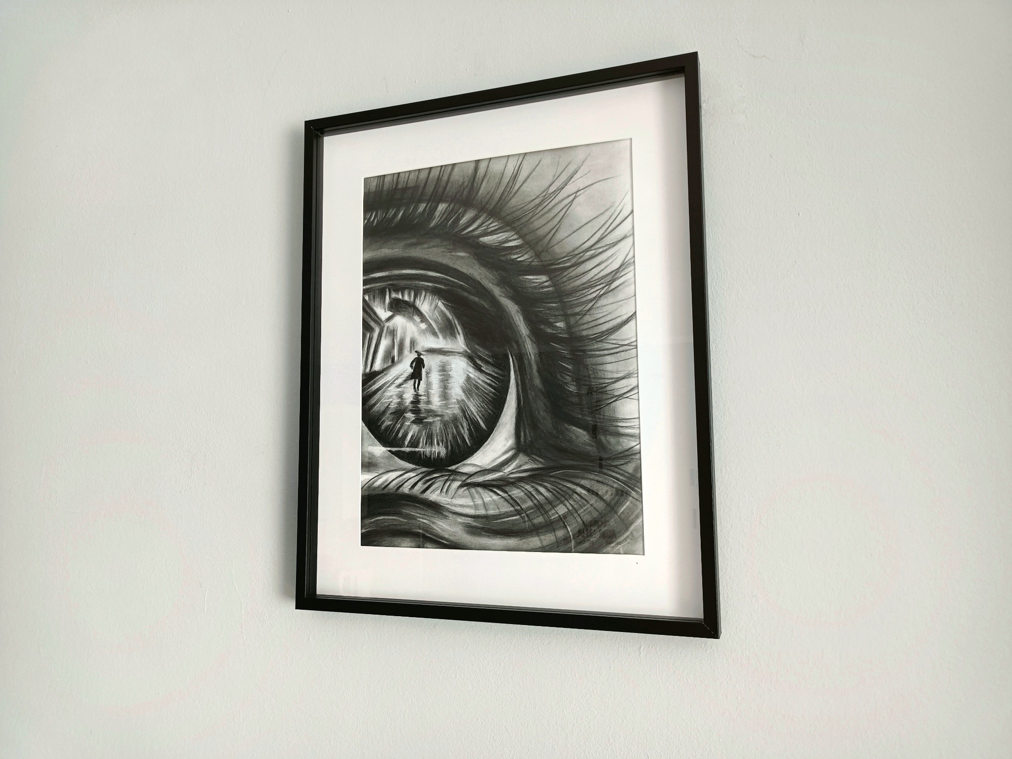 Czarno-biały rysunek w ramce przedstawiający oko, w którego źrenicy odbija się postać idąca po mokrej ulicy w deszczu.