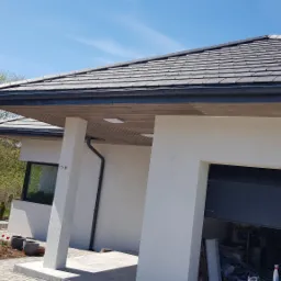 Nowoczesny dom jednorodzinny z szarą dachówką i białymi ścianami, widok z zewnątrz na częściowo otwarty garaż i zadbany ogród z tulipanami.