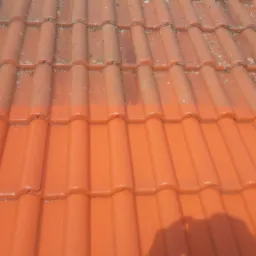 Częściowo oczyszczona czerwona dachówka, widoczna wyraźna różnica między brudną i umytą powierzchnią, cień w prawym dolnym rogu.