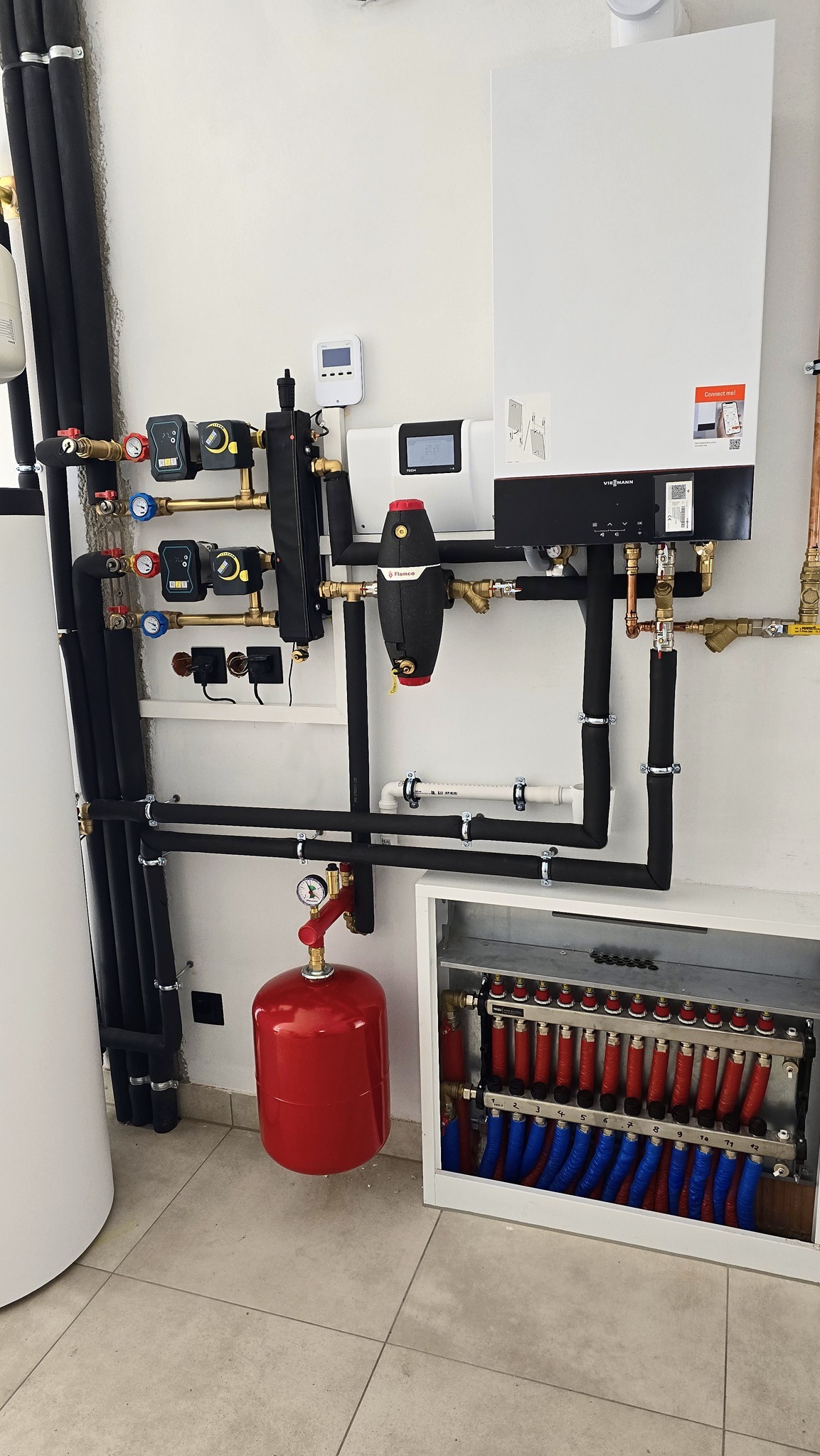 Kompleksowa instalacja centralnego ogrzewania z kotłem Viessmann, rozdzielaczem podłogowym z czerwono-niebieskimi pętlami, czarnymi rurami izolowanymi, czerwonym zbiornikiem wyrównawczym i filtrem...